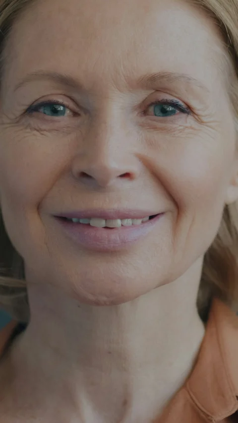 A smiling woman with blue eyes and blonde hair in an orange shirt