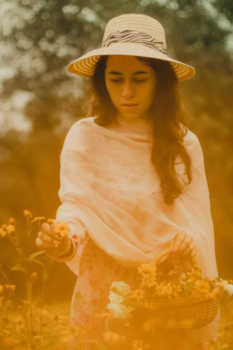 woman in white long sleeve shirt and brown hat standing on yellow flower field during daytime
