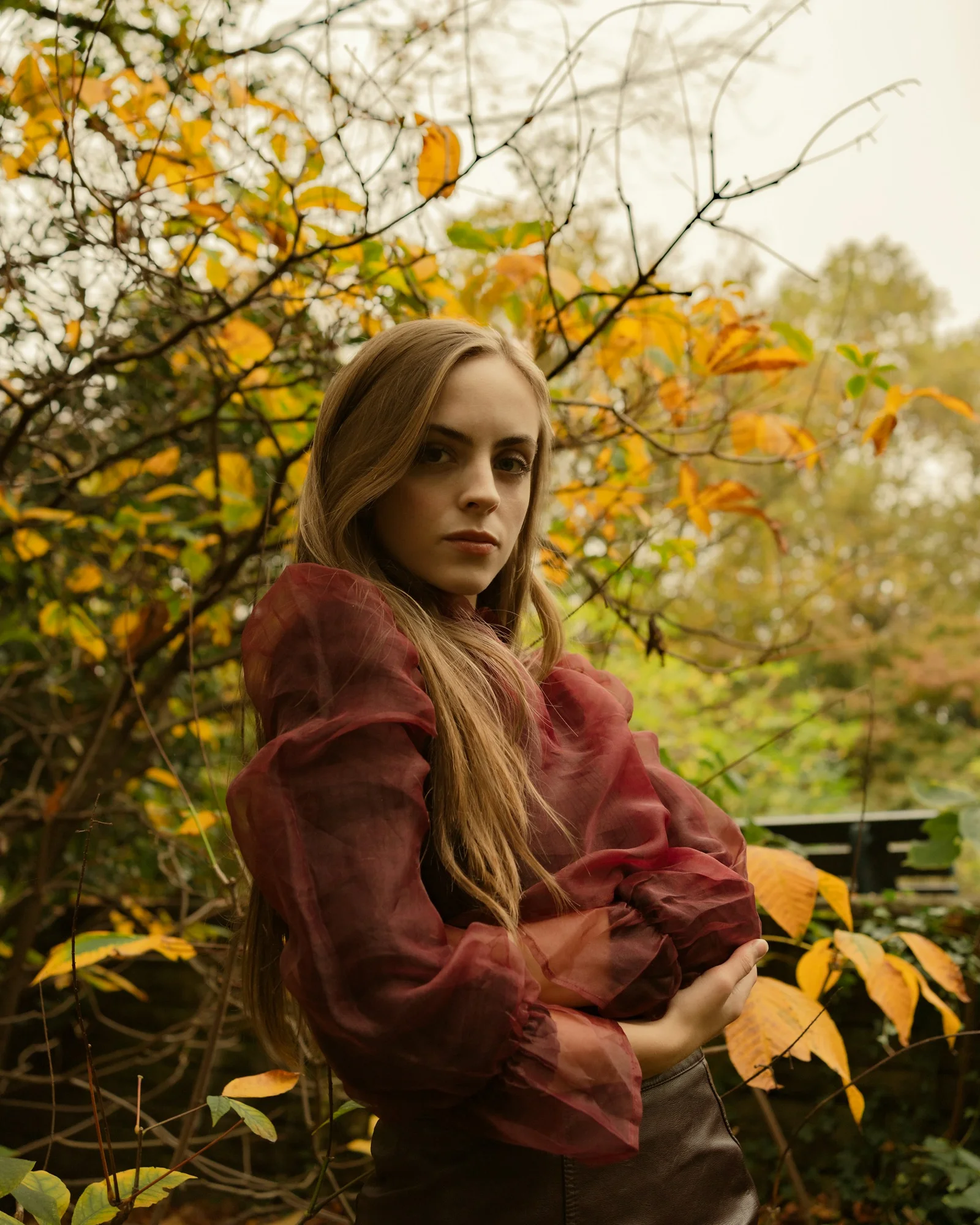 Woman in autumn leaves looks directly at the camera