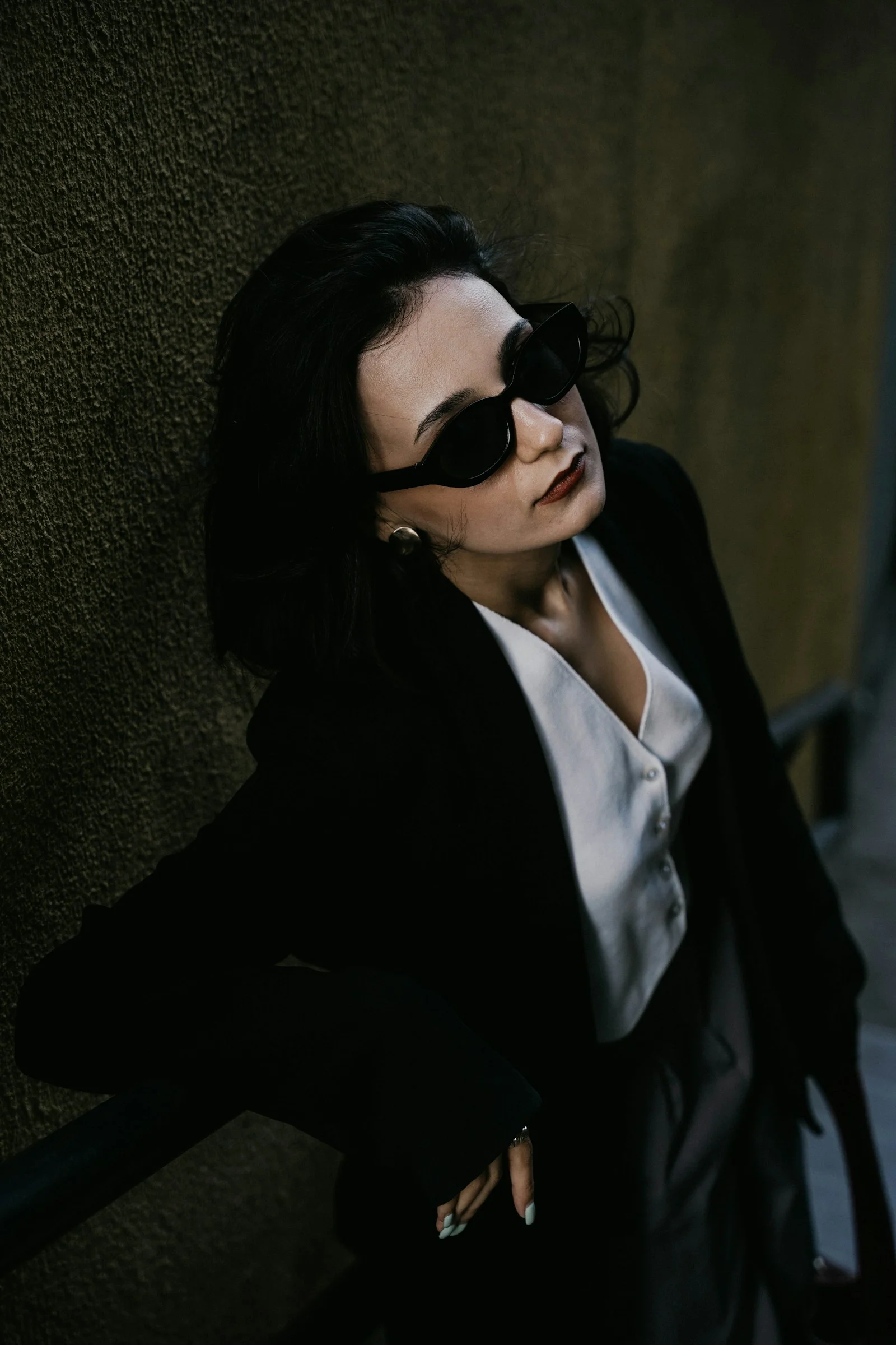 a woman in a suit and sunglasses leaning against a wall