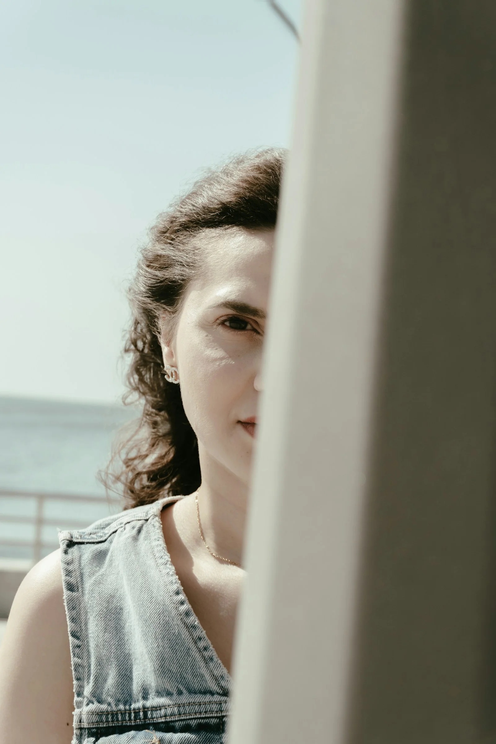 Woman with curly hair peeking, ocean visible in background