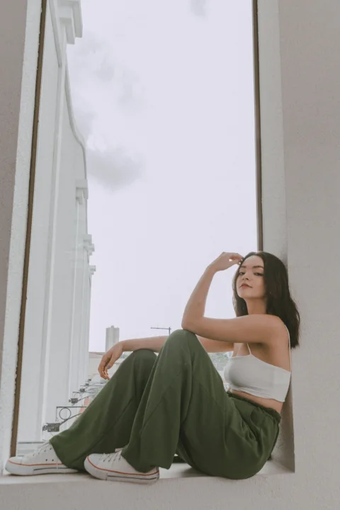 穿白色上衣和綠色褲子的女性坐在窗台上