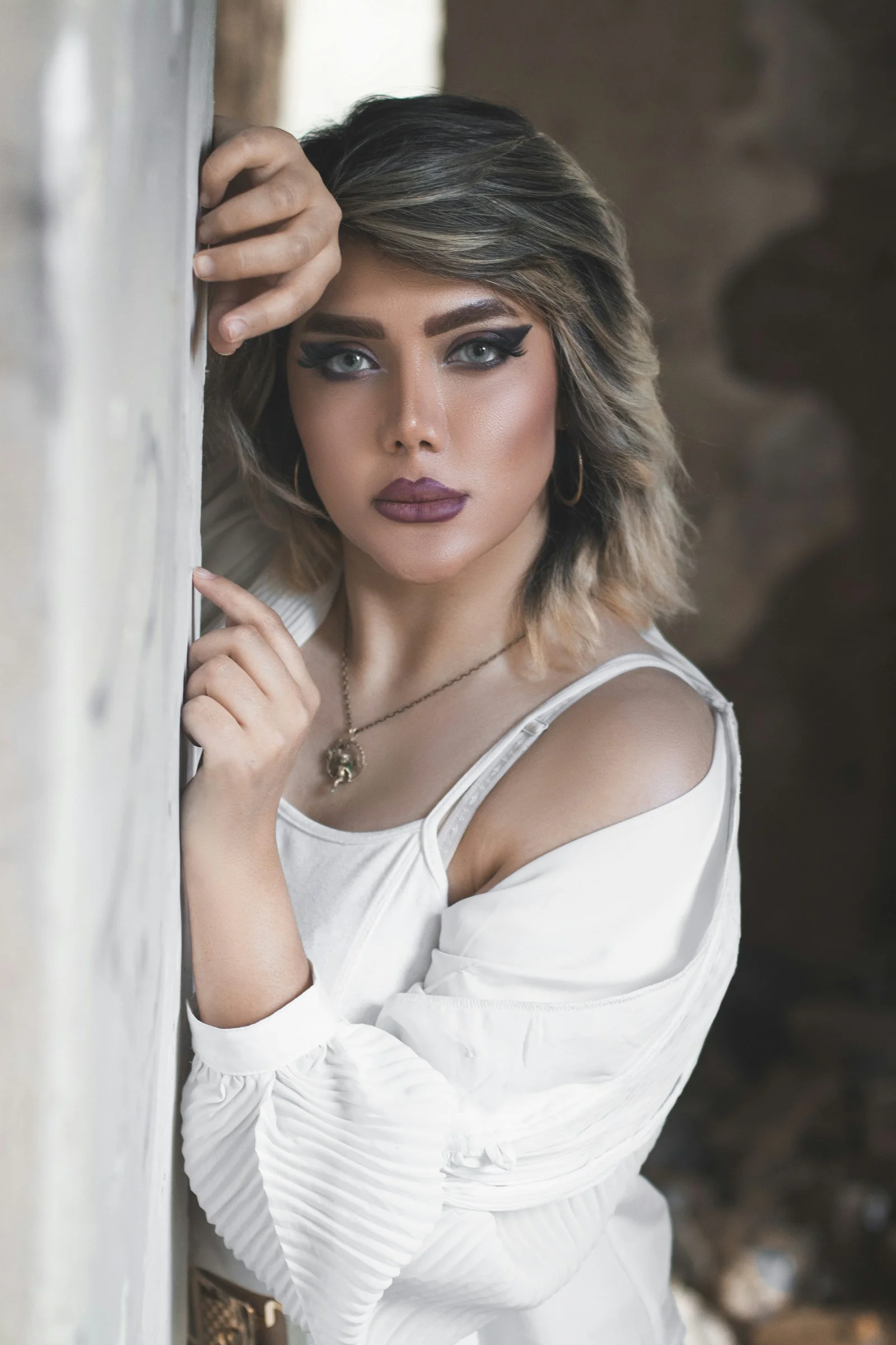 a woman in a white top leaning against a wall