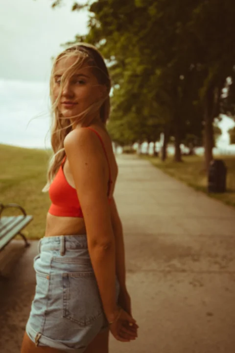 白天，一名身穿紅色運動內衣和藍色牛仔短褲的女子站在灰色水泥路上