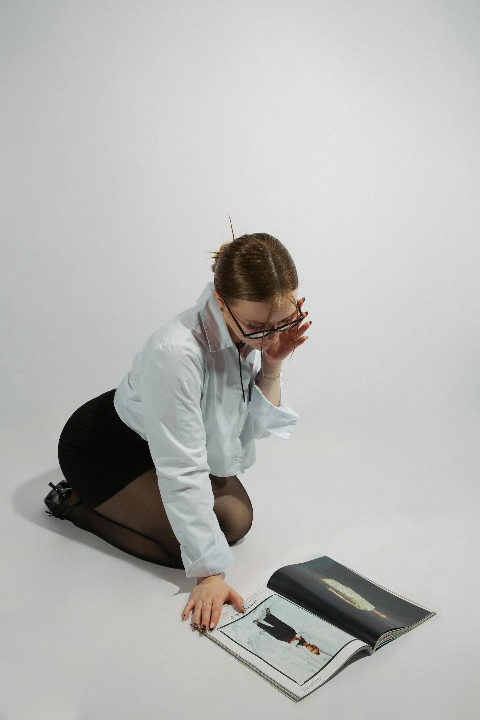 A woman kneels, reading a magazine