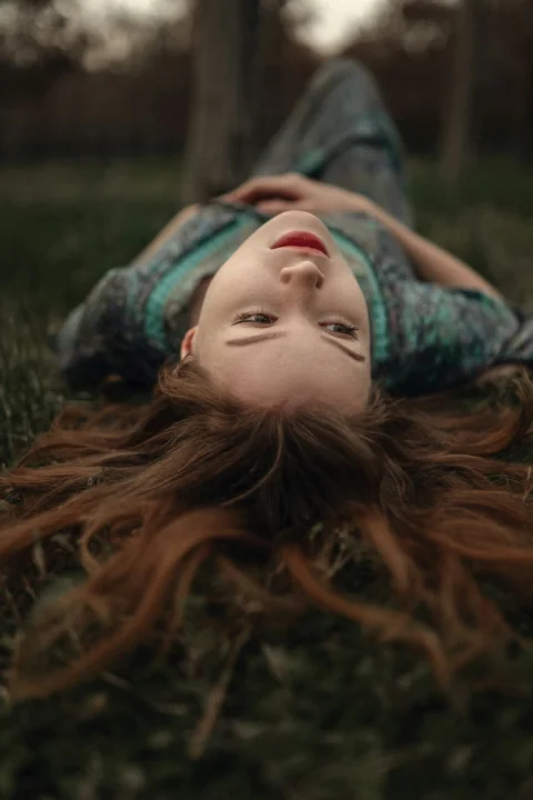 a young girl laying on the grass with her hair blowing in the wind