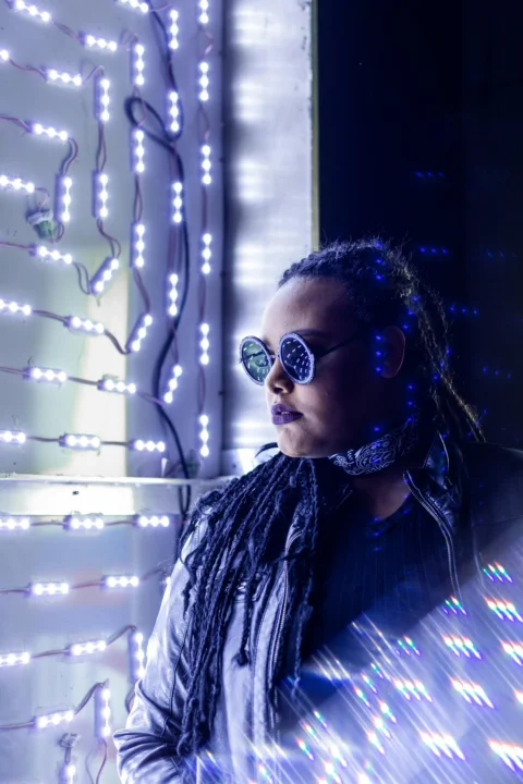 a woman wearing sunglasses and a scarf standing in front of a wall with lights