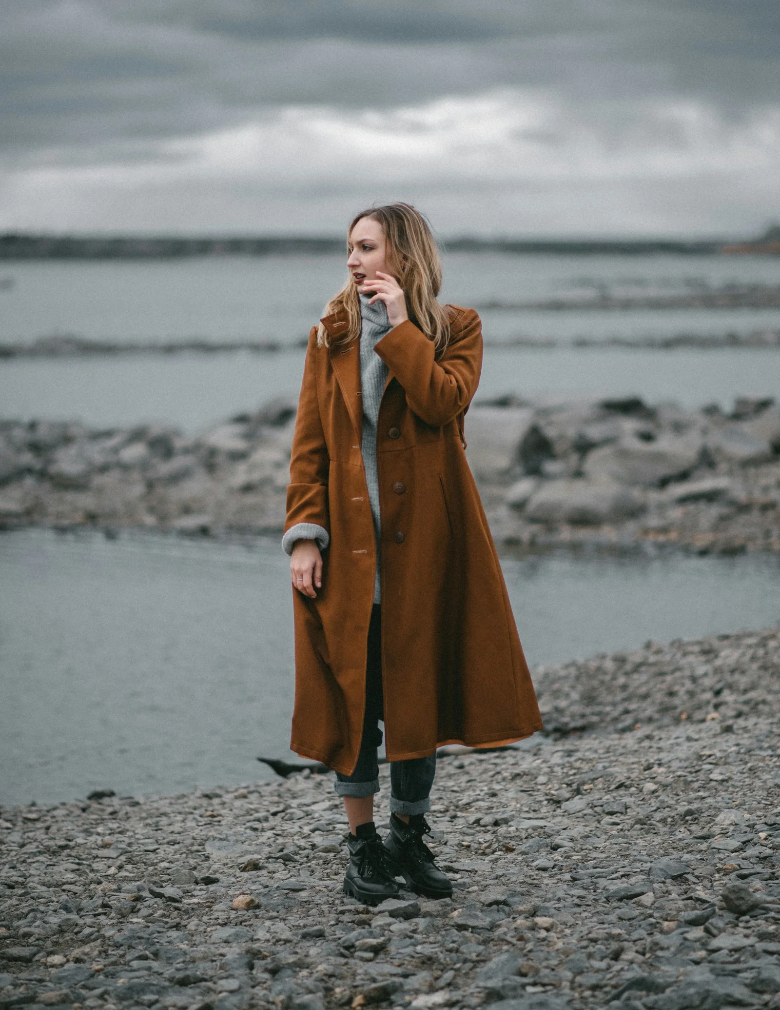 a person in a long coat on a rocky beach