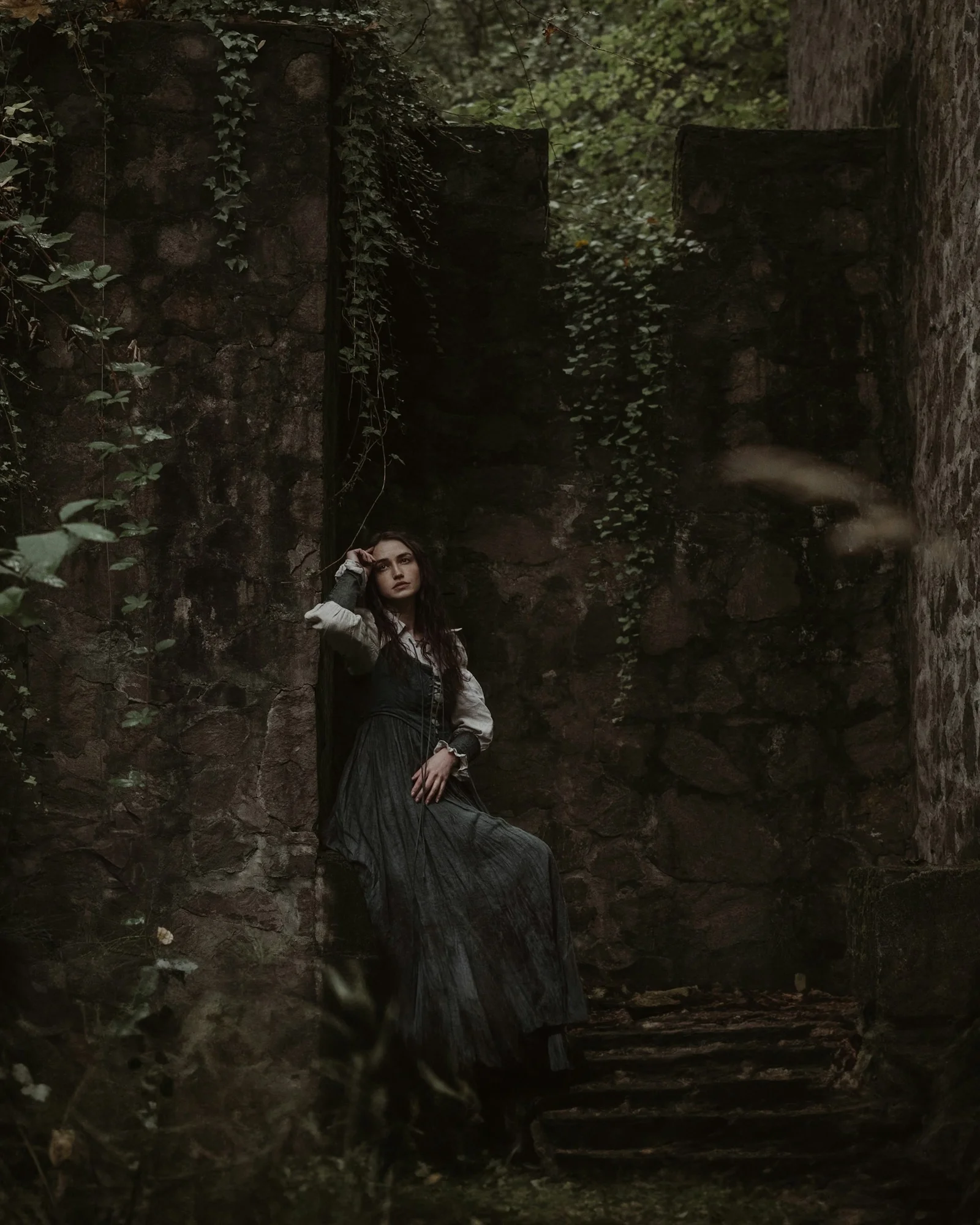 a woman in a black dress is sitting on a stone staircase