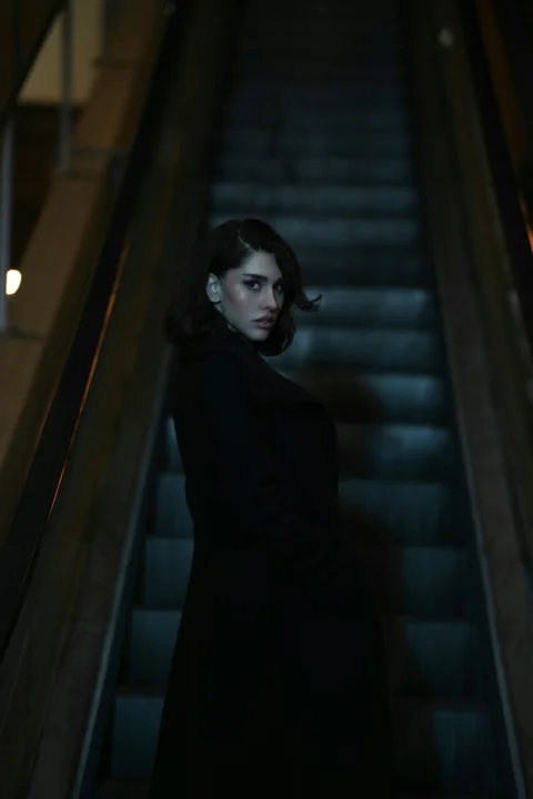 A woman stands on a dark escalator