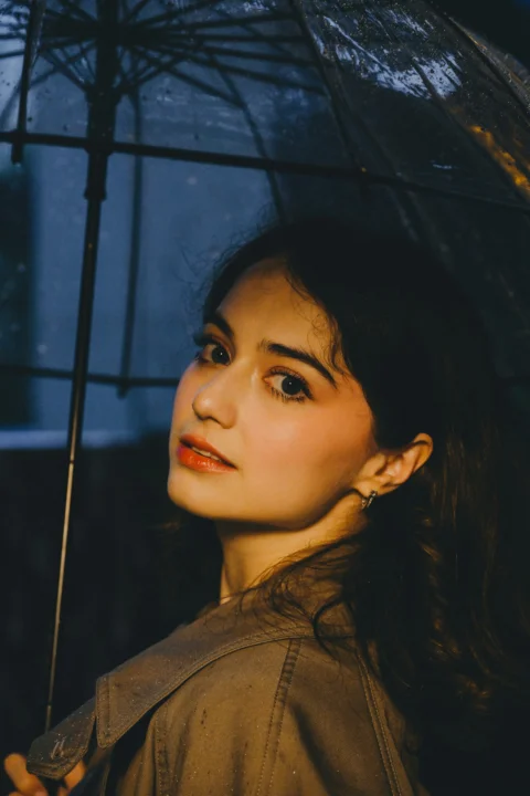 A woman looking back under a clear umbrella in the rain at night