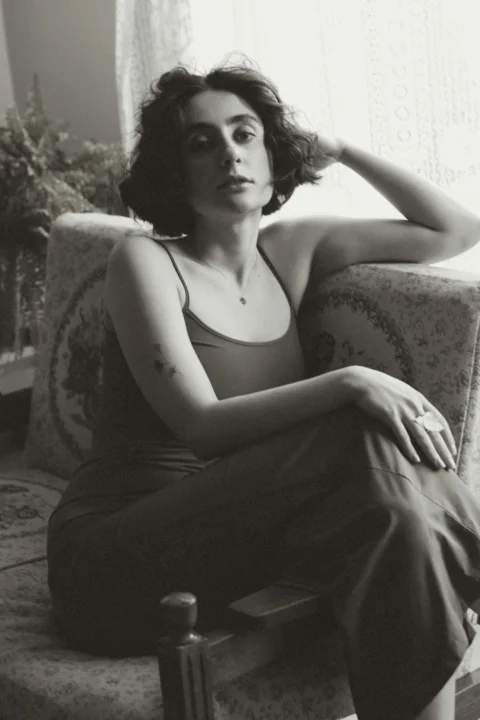 A woman with short dark hair sitting on a patterned armchair in soft light