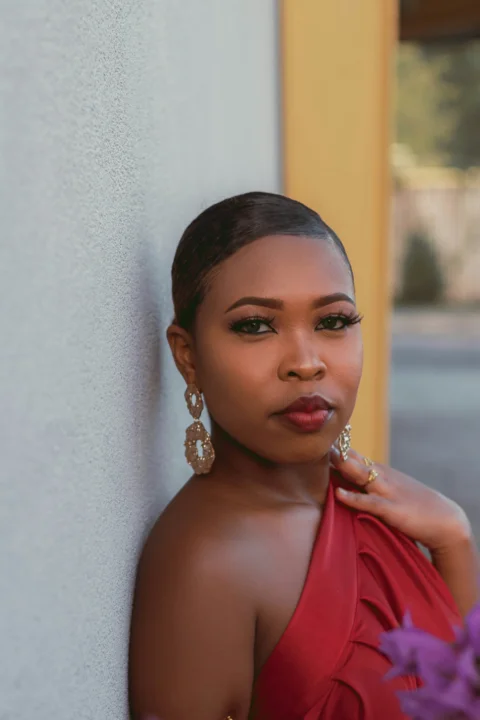 a woman in a red dress leaning against a wall