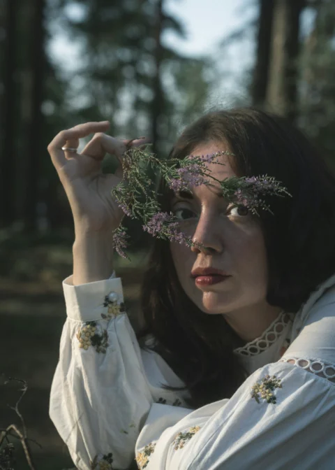 Woman holding flowers over her eyes in forest