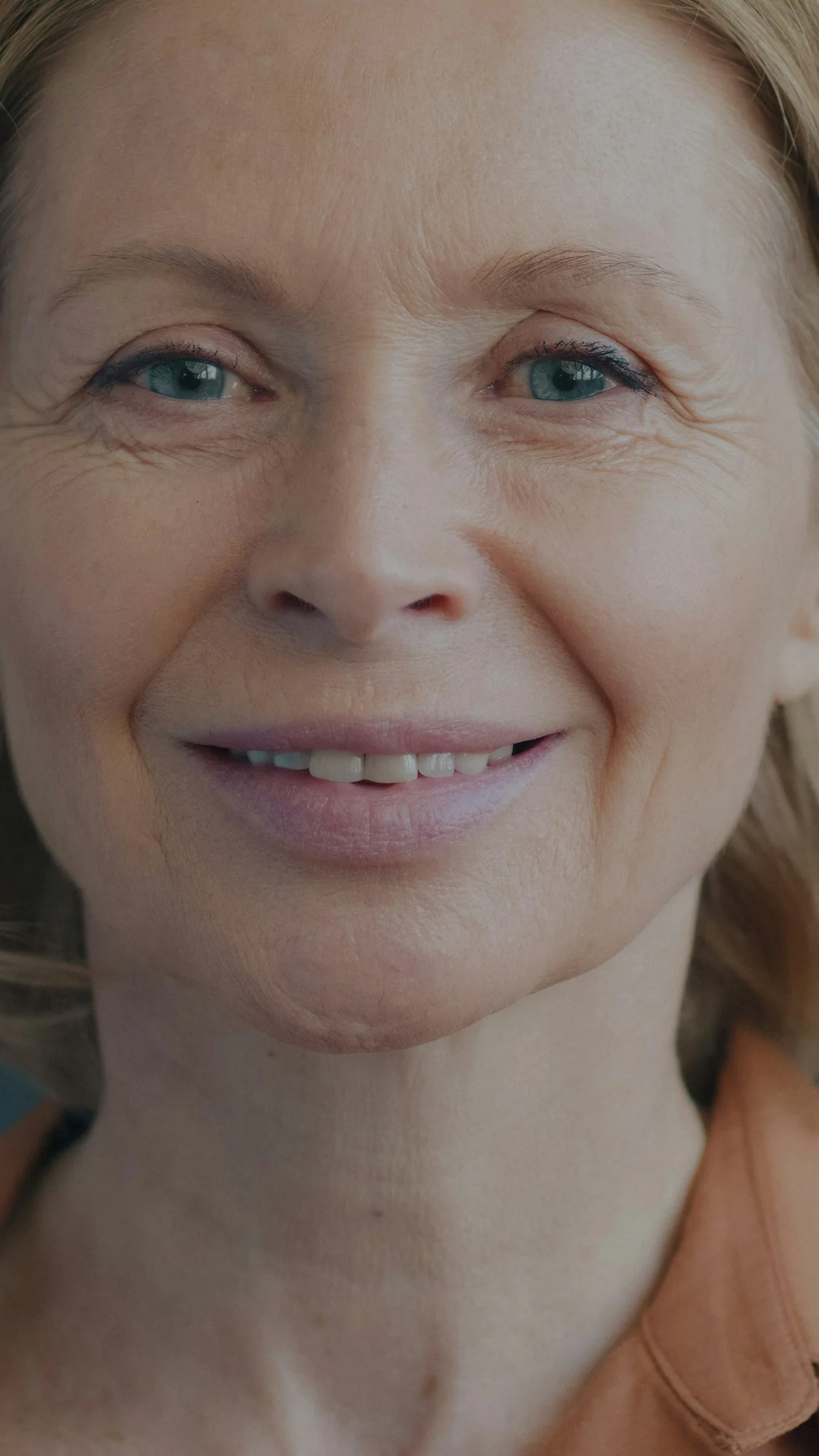 A smiling woman with blue eyes and blonde hair in an orange shirt