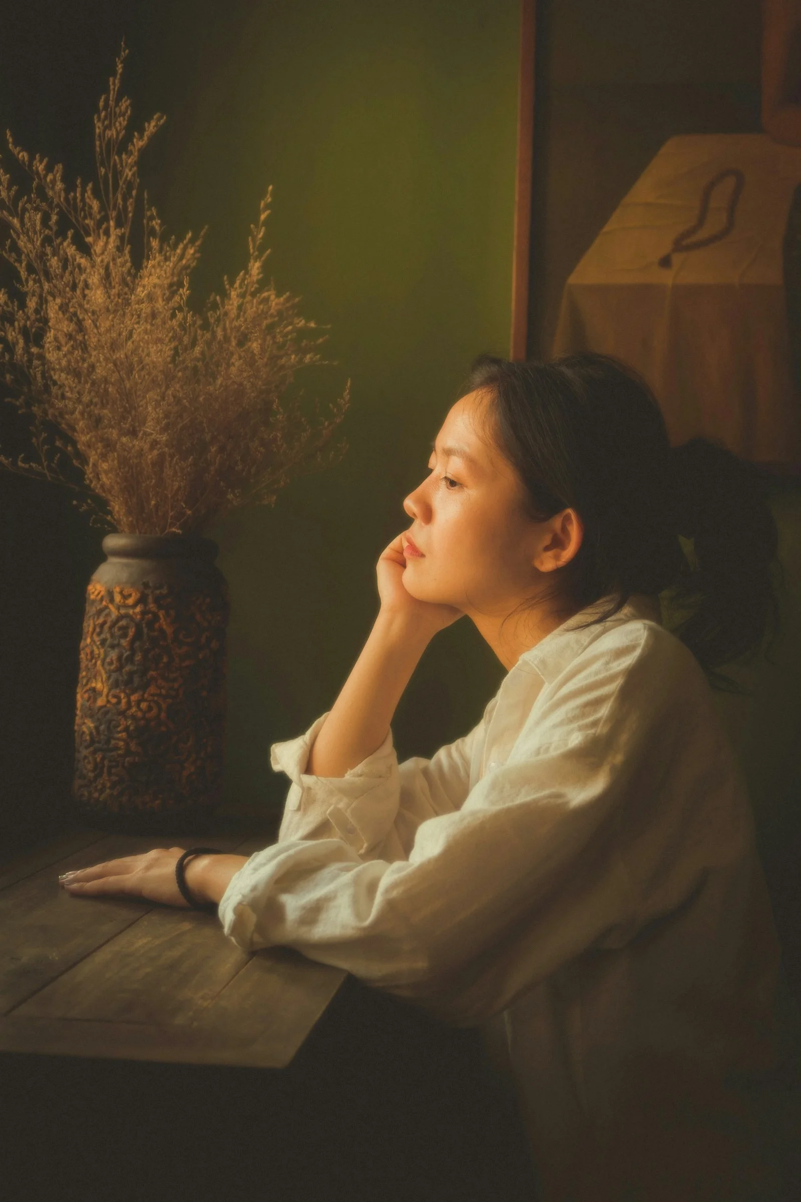女子坐在桌旁，桌上放着一瓶花