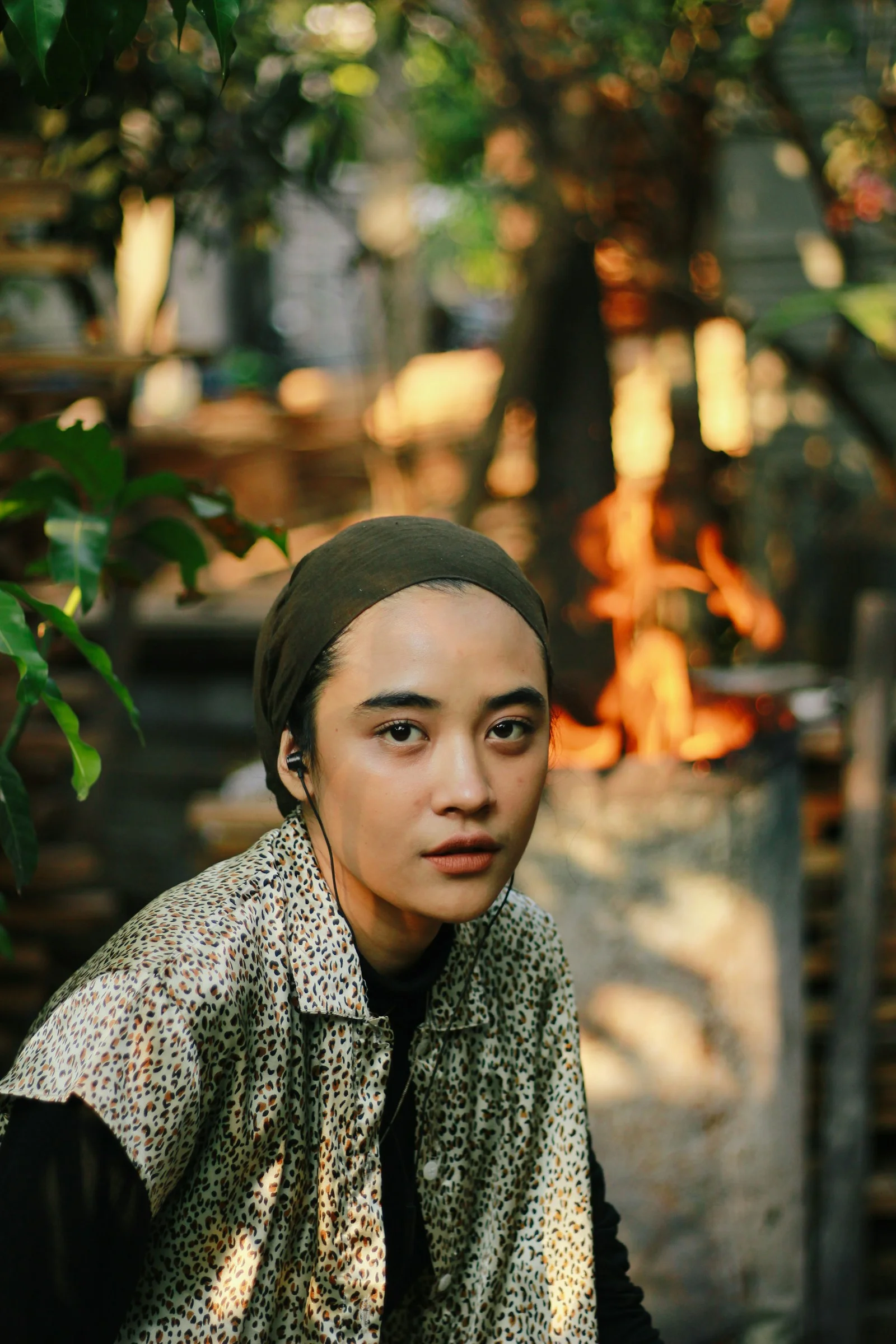 A young person with earbuds looks at the camera outdoors