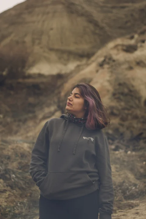 a woman in a black hoodie standing in front of a mountain