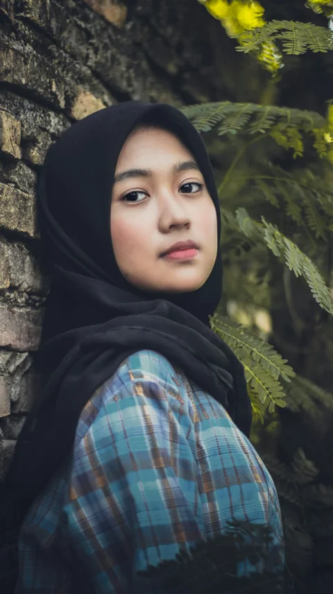 파란색과 갈색 체크 무늬 아바야 드레스를 입고 검은 히잡 스카프를 쓴 여성