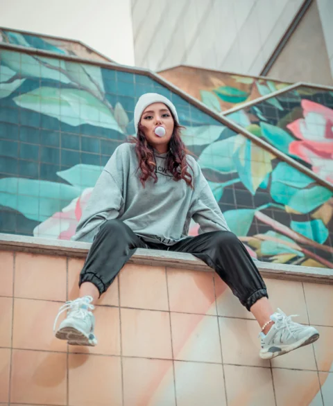 Young woman blows bubblegum sitting on a tiled wall