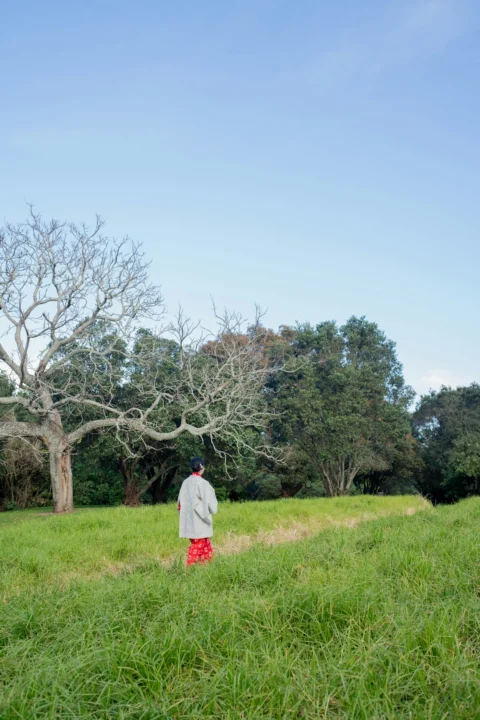 Person walking in grassy field with trees and blue sky