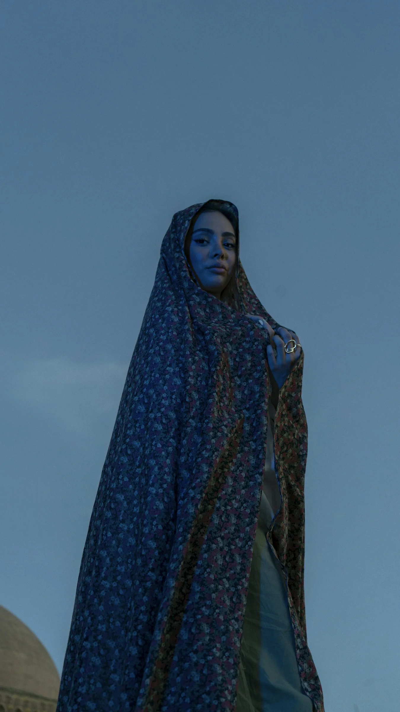 A woman in a headscarf stands under a blue sky