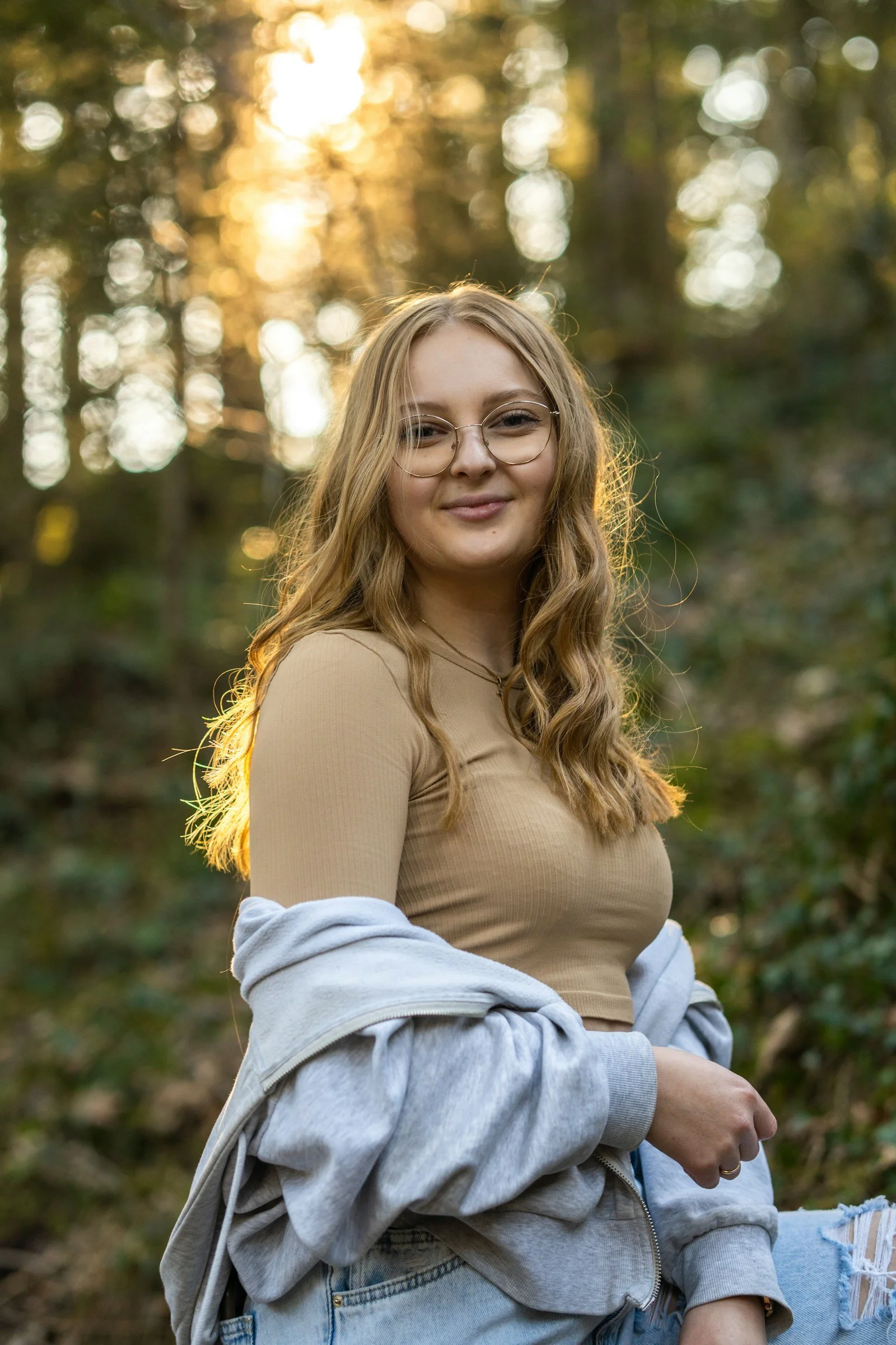 a woman with glasses sitting on a log in the woods