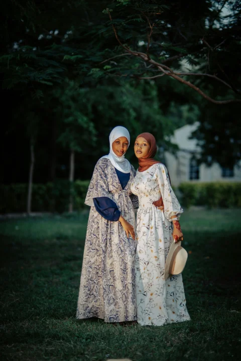 Two women in hijabs and dresses pose outdoors