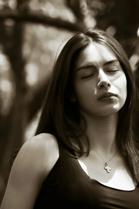 Serene young woman with closed eyes in dappled light