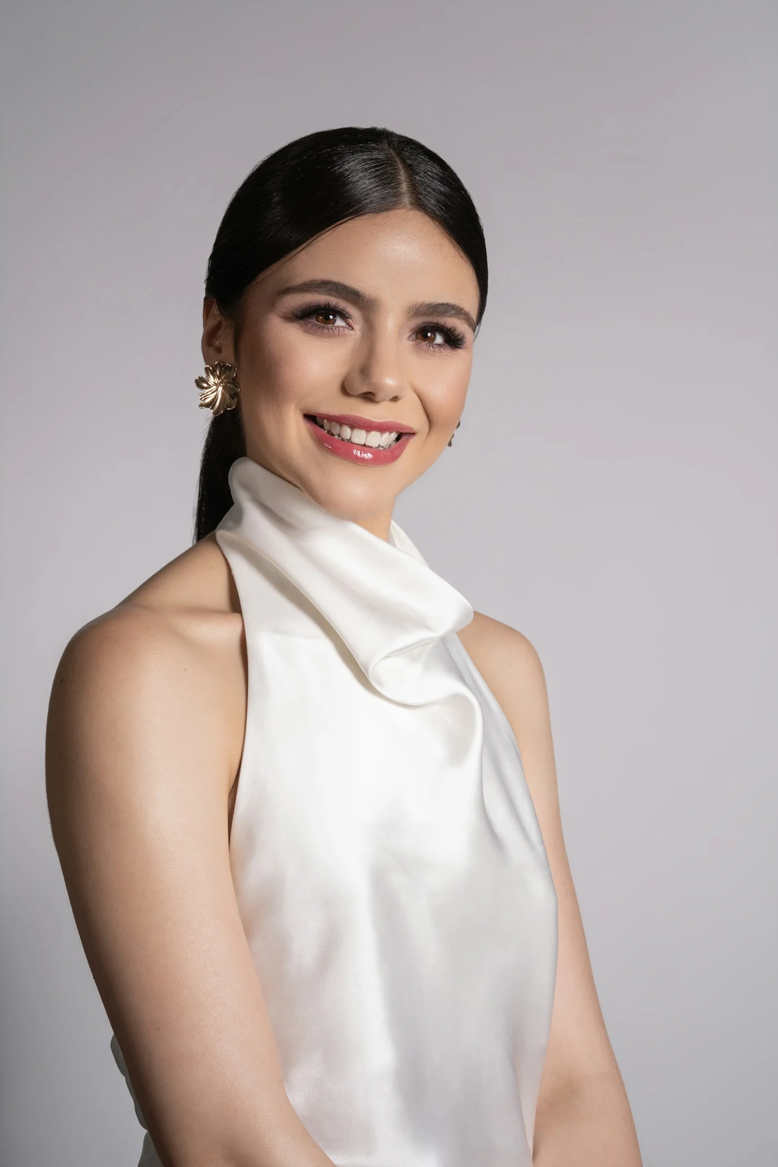 A woman with dark hair in a ponytail wearing a white satin halter top
