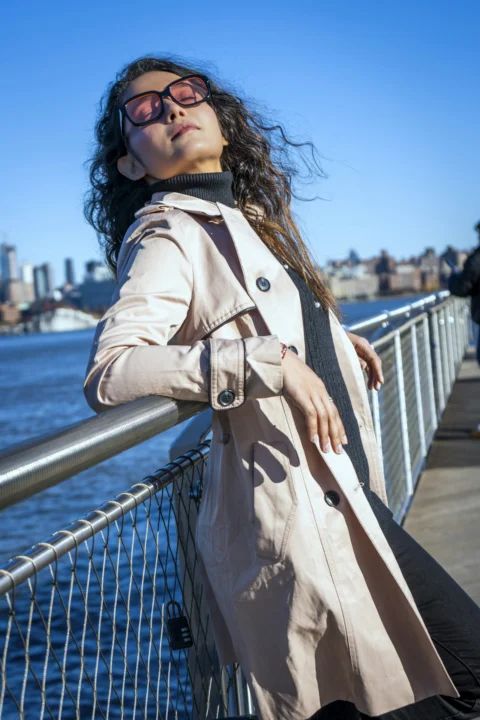 a woman in a trench coat leaning on a fence