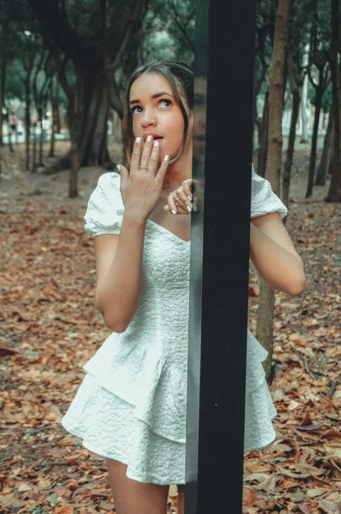 a woman in a white dress holding her hand up to her face