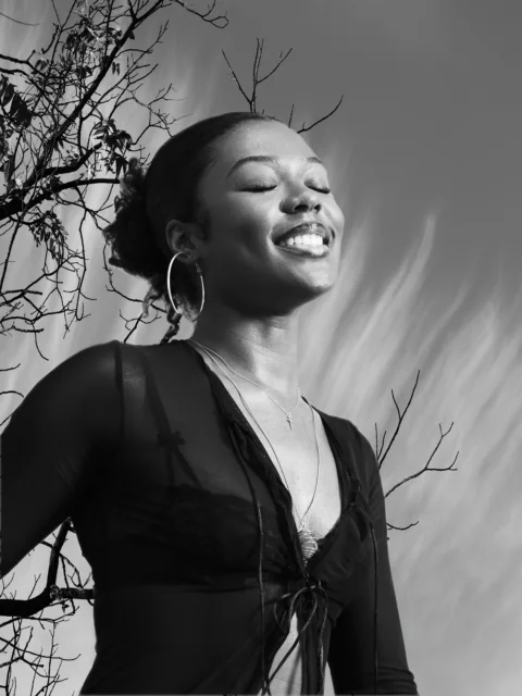Young woman with eyes closed, smiling against sky