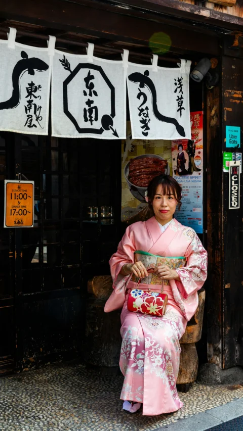 Woman in pink kimono sits outside a japanese restaurant