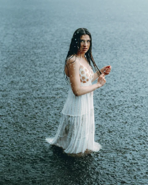 Woman stands in the rain wearing a white dress