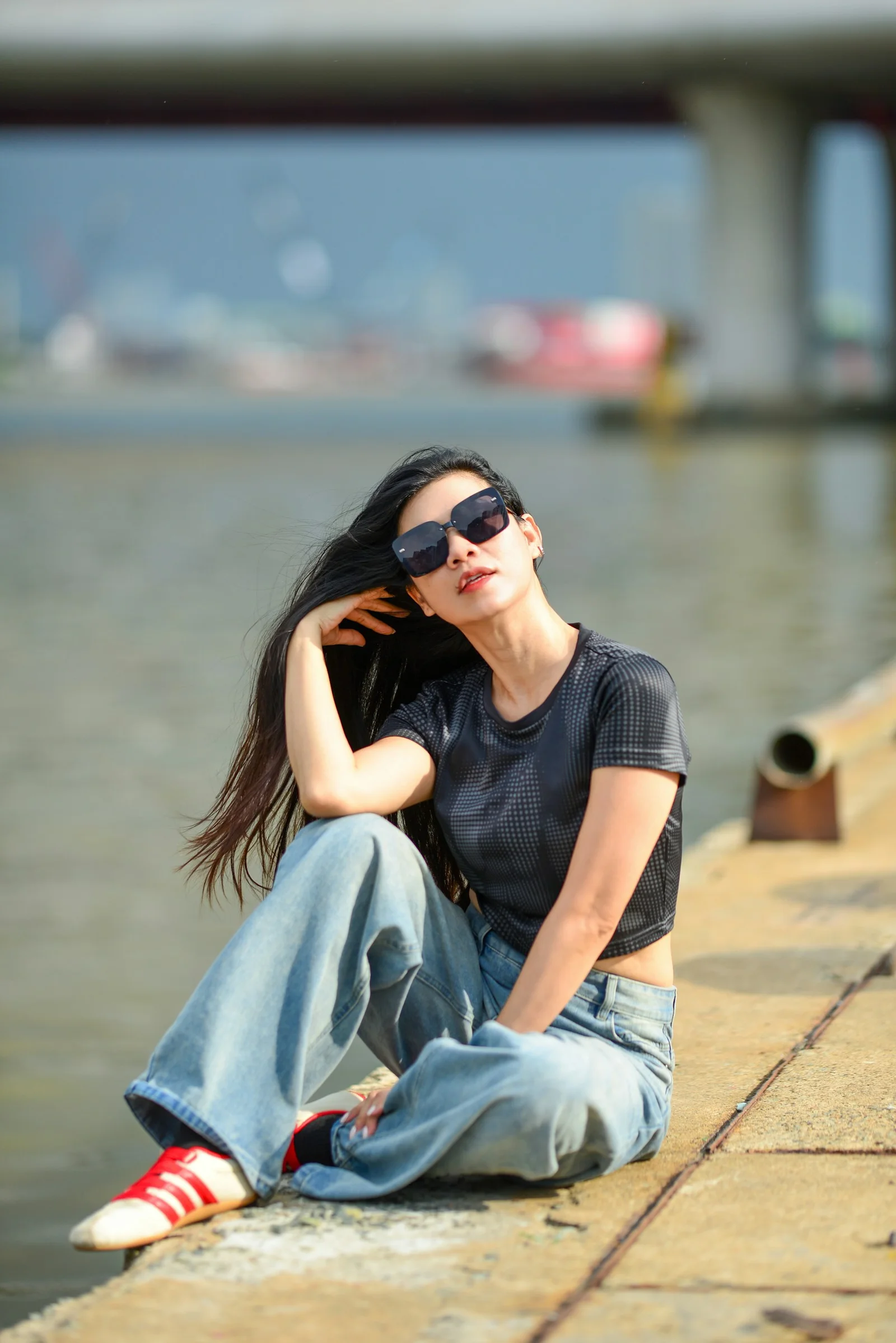 A woman in sunglasses and a black top sitting on a concrete pier