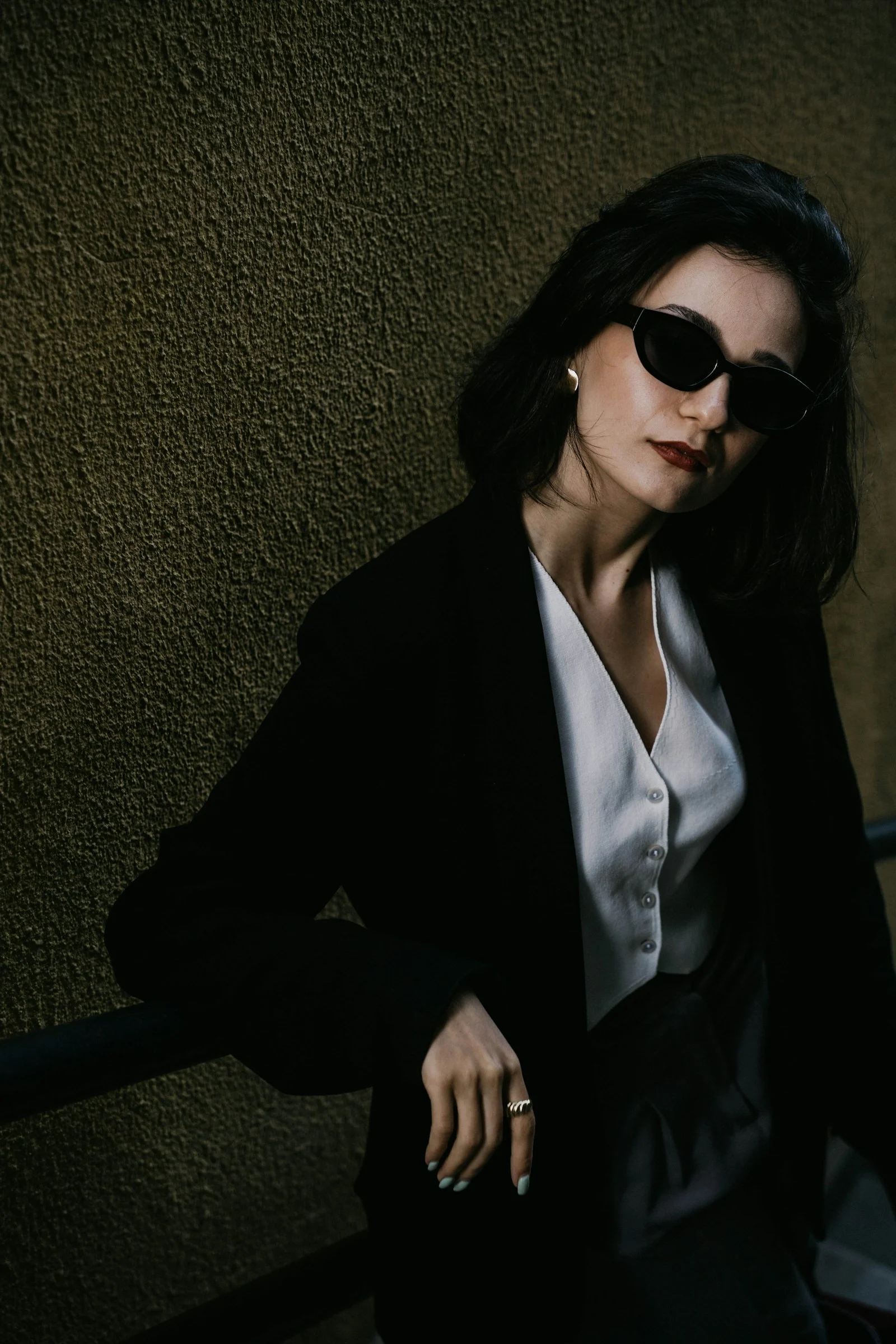 a woman in a suit and sunglasses leaning against a wall