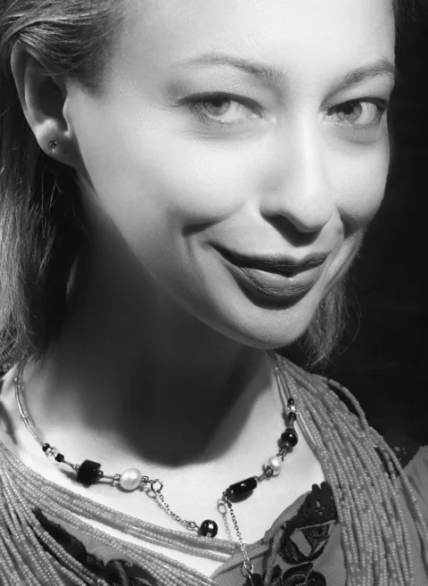 A woman with a subtle smile wearing a beaded necklace