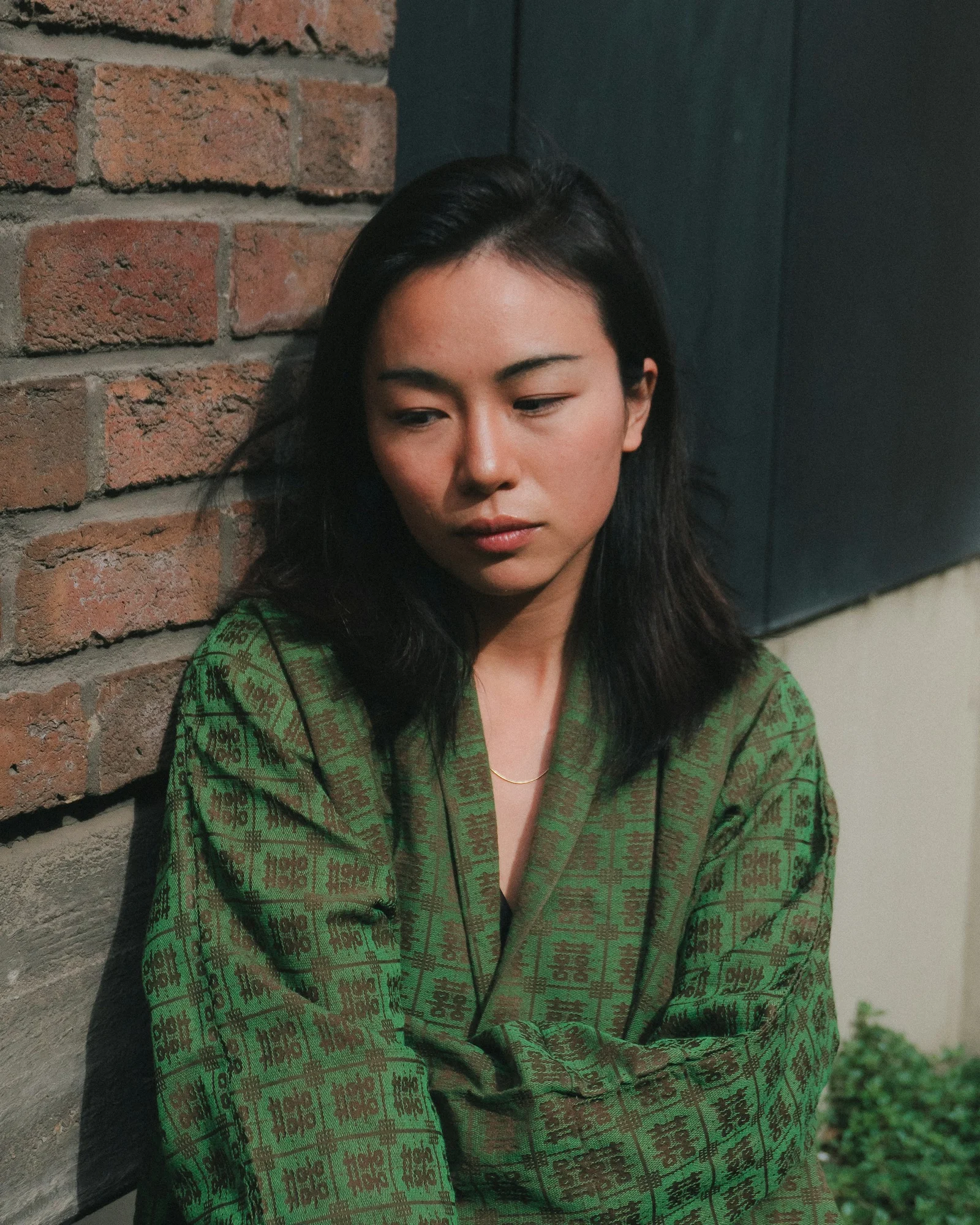 Young woman in green robe leans against brick wall