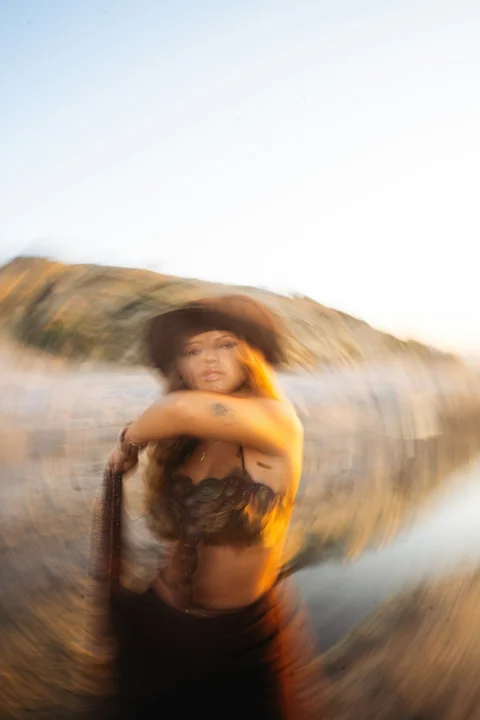 A woman in a brown hat and fur top against a blurred coastal landscape