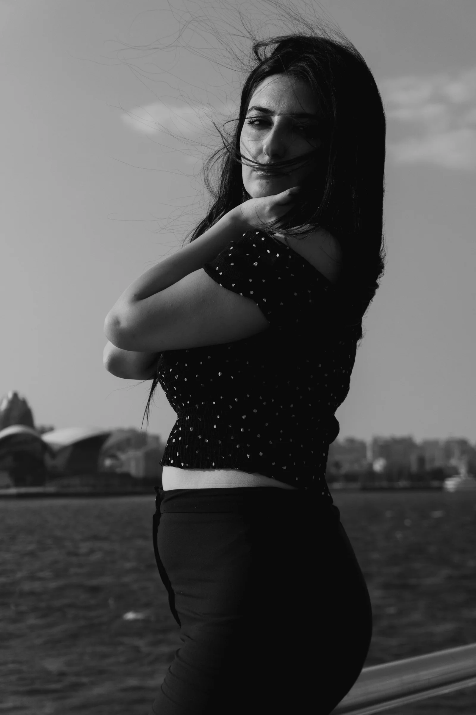 A woman in a polka dot top standing by a river with city buildings