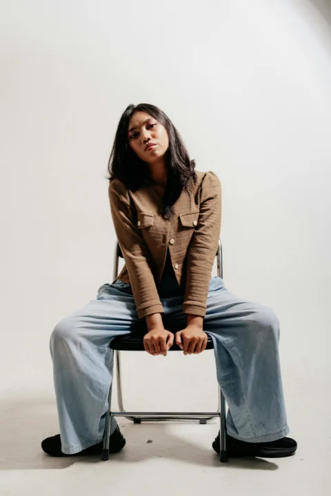 A woman in a brown jacket sits on a chair