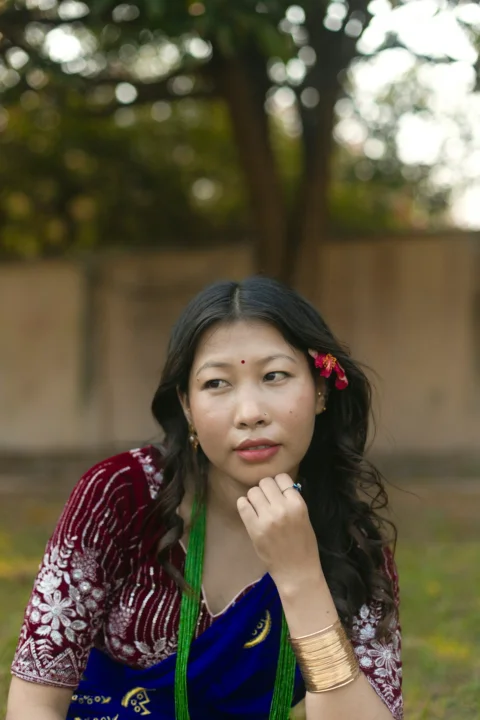 A woman in a maroon embroidered blouse and blue sari with a flower in her hair