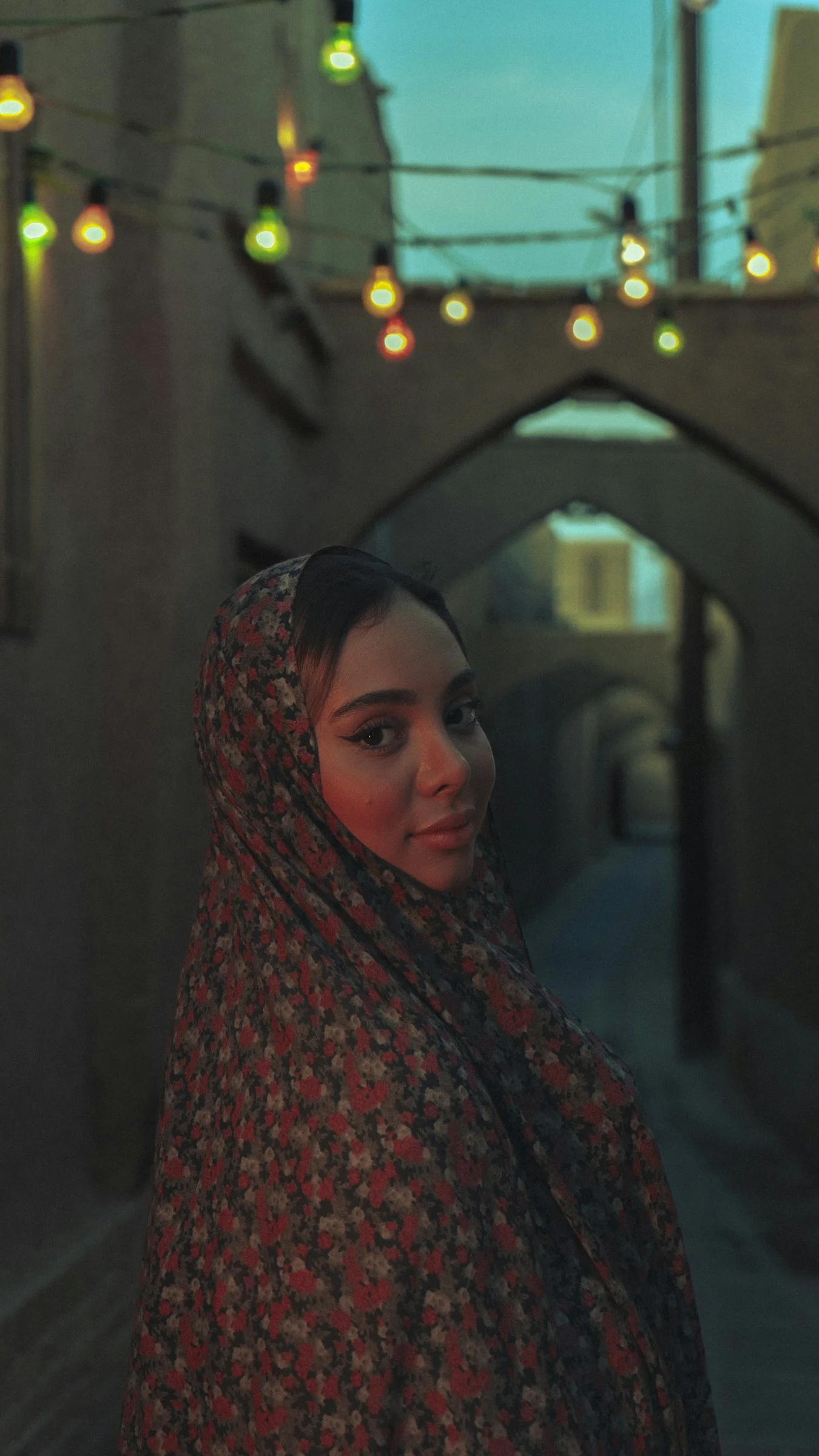 A woman wearing a headscarf in a dimly lit alley
