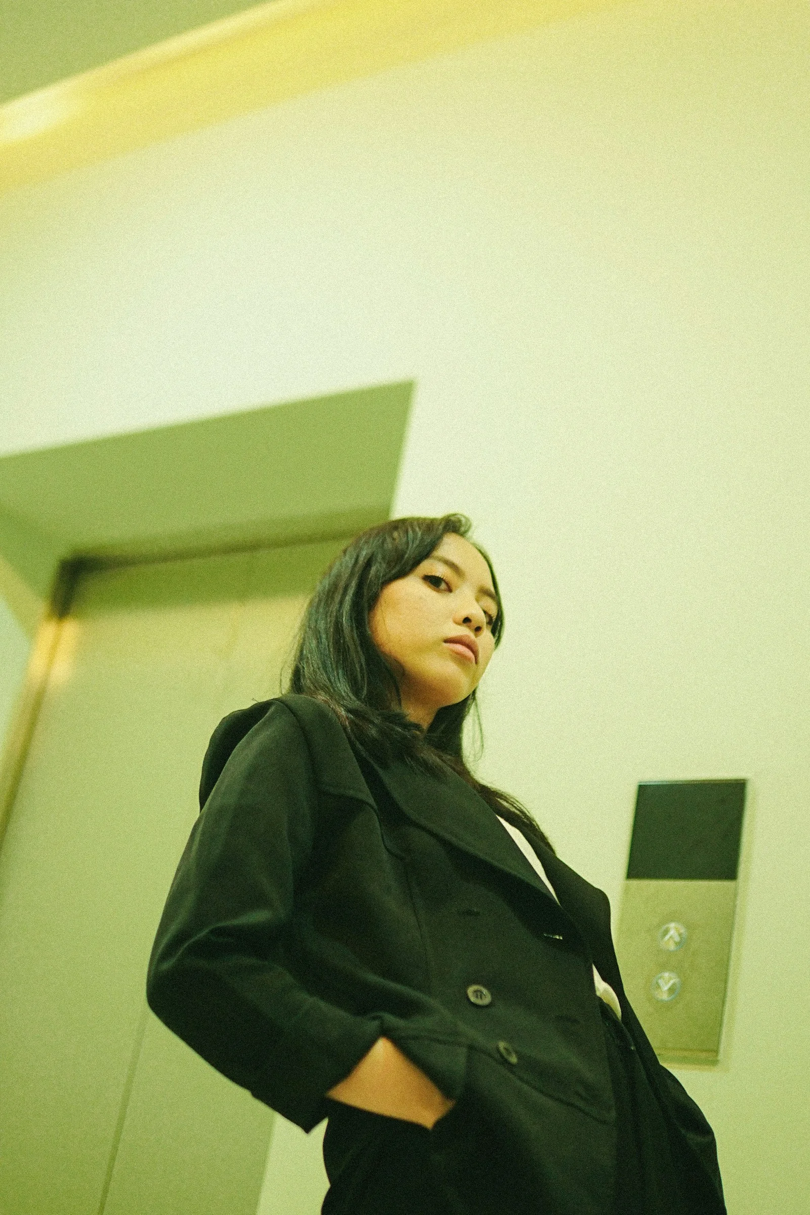 白い壁のそばに立つ黒いコート姿の女性