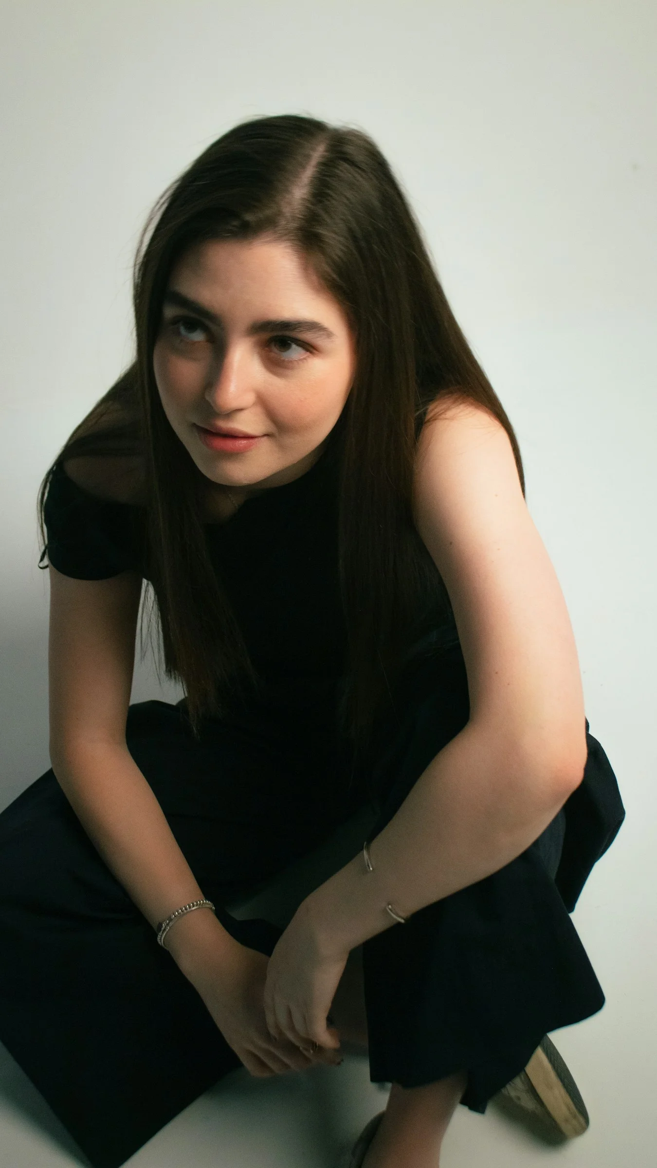 Young woman in black clothing crouching on a white background