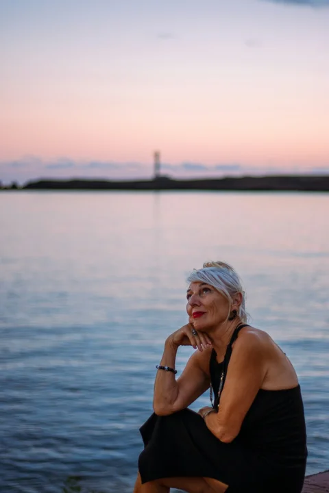 Woman looking up at a pastel sunset over water