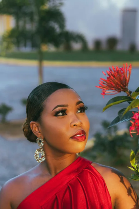 a woman in a red dress standing next to a flower