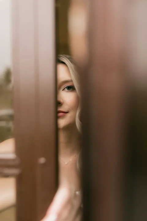 Blonde woman peeking from behind a brown door frame