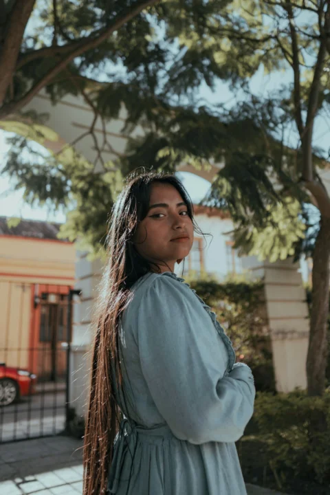 A woman poses outside underneath trees